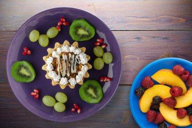 Kek ve meyve üzümleri, kivi, mor ahşap arka planda nar. Mor tabak manzaralı tatlı.