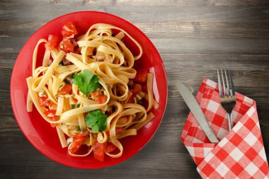 Çatal ve bıçak manzaralı kırmızı tabakta spagetti. domatesler, soğanlar, siyah ahşap arka planda lahana.