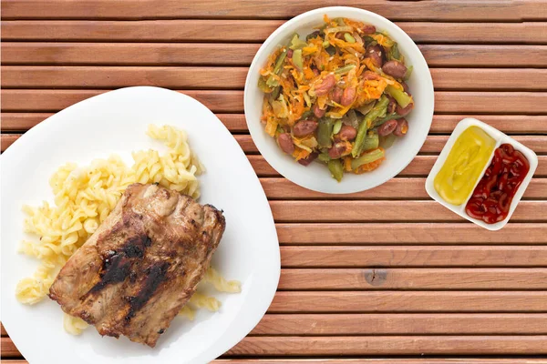 grilled pork ribs with pasta. grilled pork ribs on a white plate on a orange wooden background. grilled pork ribs top view