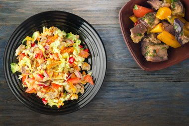 Tavuk mideli salata ile sebze havuç, soğan, biber, lahana, domates, brokoli. Mavi ahşap arka planda siyah tabakta tavuklu salata. Vejetaryen salata üstü görünümü.