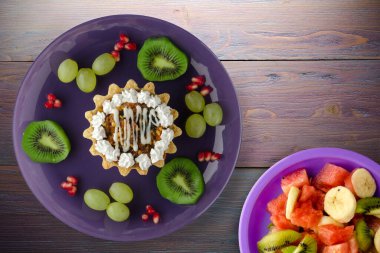 Kek ve meyve üzümleri, kivi, mor ahşap arka planda nar. Mor tabak manzaralı tatlı.