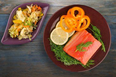 Kahverengi tabakta, vejetaryen salata manzaralı kırmızı balık filetosu. Mavi ahşap arka planda balık alabalığı. Dereotu, limon ve biberli alabalık.