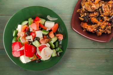 Yeşil ahşap arka planda Yunan salatası. Vejetaryen salata manzaralı yeşil tabakta Yunan salatası. sağlıklı yiyecekler
