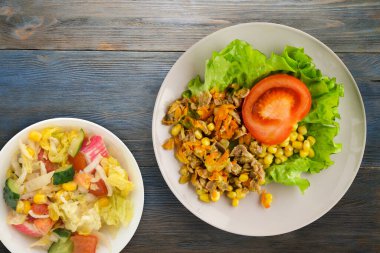 Tavuk mideli salata, havuç, mısır ve açık gri tabakta salata. Mavi ahşap arka planda sebzeli tavuk salatası.