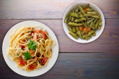 Vejetaryen salata manzaralı beyaz tabakta spagetti. domatesler, soğanlar, lahanalar mor ahşap arka planda.
