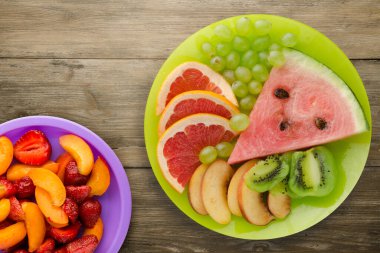 Doğuştan ahşap arka planda kesilmiş meyve. Açık yeşil bir tabakta dilimlenmiş meyve ince zeka meyveleri mor bir tabakta.