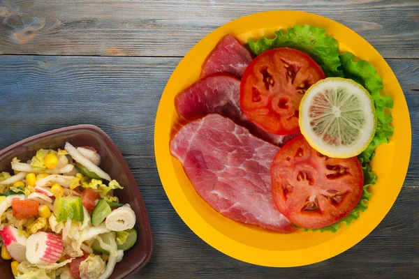 ham with salad, tomato and lemon on a yellow plate. ham on a blue wooden background .ham with vegetable salad  top view