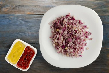 Mavi gri ahşap arka planda kırmızı soğan. Beyaz tabakta doğranmış kırmızı soğan ve soslu üst görünüm.