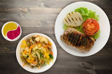 Siyah ahşap arka planda patates ve domatesle ızgara domuz eti. Salata soslu ızgara domuz eti.