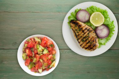 grilled chicken fillet with vegetables lemon, salad, onion on a green wooden background. chicken fillet grilled on a white plate top view