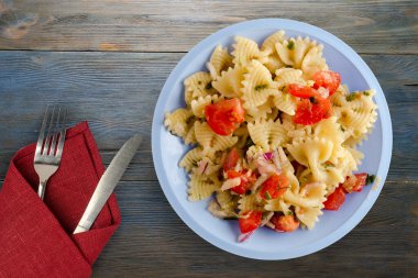 Çatal ve bıçak manzaralı açık mavi tabakta makarna. makarnalar, domatesler, soğanlar, lahanalar mavi ahşap arka planda