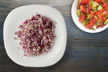 Mavi gri ahşap arka planda kırmızı soğan. Beyaz tabakta doğranmış kırmızı soğan ve vejetaryen salata.