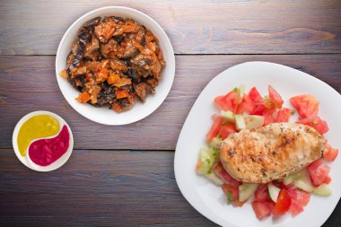 Domates salatası, salatalık ve soğanlı ızgara tavuk göğsü. Mor ahşap arka planda beyaz tabakta ızgara tavuk göğsü. Kızarmış tavuk göğsü manzaralı. Düz yatıyordu.