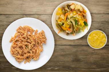 Tahta arka planda izole edilmiş beyaz bir tabakta makarna. Dereotlu domates soslu makarna. salata soslu makarna.