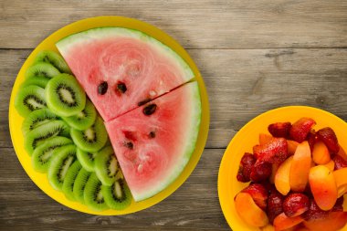 Karpuz ve kivi kahverengi ahşap bir arka planda sarı bir tabakta dilimlenmiş. Karpuz ve meyvelerle dilimlenmiş kivi.