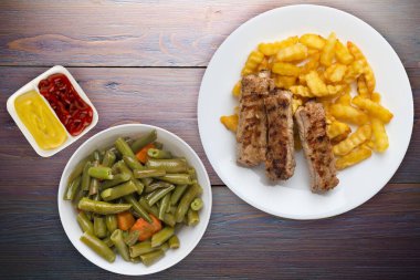 Beyaz tabakta domuz pirzolası ve patates, sebze salatası ve mor ahşap arka planda sos. Fast food 'un en iyi manzarası. Sağlıksız yiyecekler.