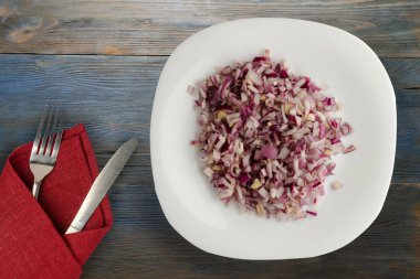 Mavi gri ahşap arka planda kırmızı soğan. Çatal ve bıçak manzaralı beyaz tabakta doğranmış kırmızı soğan.