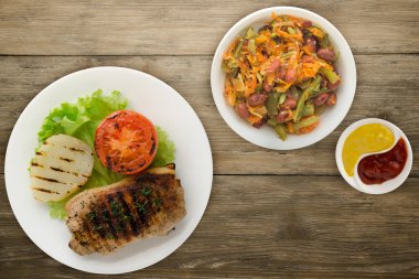 pork grilled with potatoes and tomato on a wooden background. grilled pork on a white plate with salad top view