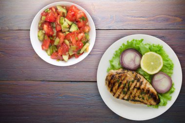 Sebzeli ızgara tavuk fileto limon, salata, mor ahşap arka planda soğan. Tavuklu fileto, beyaz tabak şeklinde ızgara.