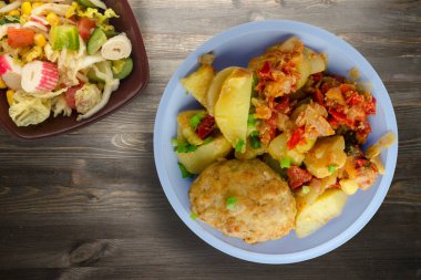 Patatesli pirzola ve fırında domates. Siyah ahşap arka planda vejetaryen salatası olan mavi bir pirzola.