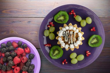 Kek ve meyve üzümleri, kivi, mor ahşap arka planda nar. Mor tabak manzaralı tatlı.