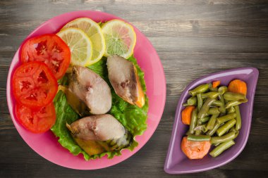 Pembe tabakta tütsülenmiş uskumru. Sebze salatanın üst manzarası. Siyah ahşap arka planda limonlu uskumru ve domates.