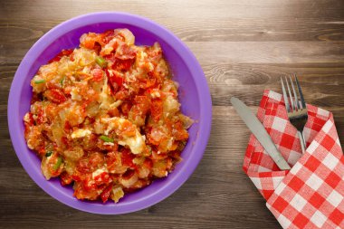 Kahverengi ahşap arka planda mor tabakta soğanlı haşlanmış domatesler. Soğan manzaralı haşlanmış domates. Çatal ve bıçakla vejetaryen yemeği