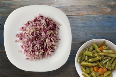 Mavi gri ahşap arka planda kırmızı soğan. Beyaz tabakta doğranmış kırmızı soğan ve vejetaryen salata.