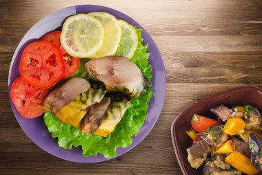 Mor tabakta tütsülenmiş uskumru. Sebze salatası manzaralı. Kahverengi ahşap arka planda limonlu uskumru ve domates.
