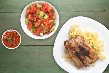 Izgara domuz pirzolası ve makarna. Yeşil ahşap arka planda beyaz tabakta ızgara domuz pirzolası. Izgara domuz pirzolası.