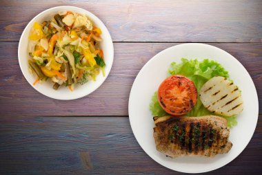 Mor ahşap arka planda patates ve domatesle ızgara domuz eti. Salata soslu ızgara domuz eti.