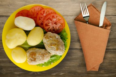 Çatal ve bıçak manzaralı sarı tabakta patatesli pirzola. Kahverengi ahşap arka planda patatesli pirzola