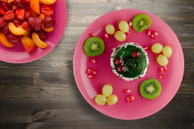 Kek ve meyve üzümleri, kivi, siyah ahşap zemin üzerinde nar. Pembe tabakta meyveli tatlı.