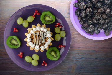 Kek ve meyve üzümleri, kivi, mor ahşap arka planda nar. Mor tabak manzaralı tatlı.