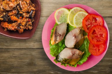 Sebze salatası manzaralı pembe tabakta tütsülenmiş uskumru. Kahverengi ahşap arka planda limonlu uskumru ve domates.