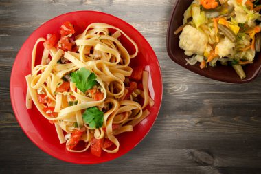 Kırmızı tabakta spagetti ve vejetaryen salata üst görüşü. domatesler, soğanlar, siyah ahşap arka planda lahana.