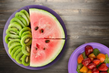 Karpuz ve kivi siyah ahşap bir zemin üzerinde mor bir tabakta dilimlendi.