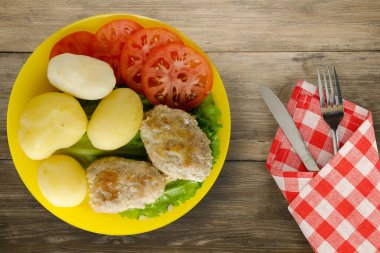 Çatal ve bıçak manzaralı sarı tabakta patatesli pirzola. Kahverengi ahşap arka planda patatesli pirzola