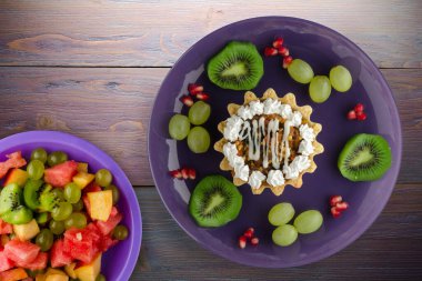 Kek ve meyve üzümleri, kivi, mor ahşap arka planda nar. Mor tabak manzaralı tatlı.