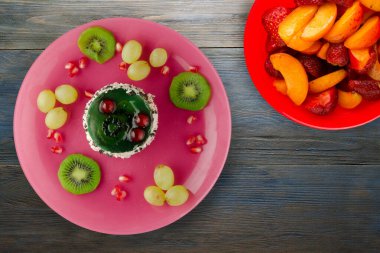 Kek ve meyve üzümleri, kivi, mavi ahşap zemin üzerinde nar. Tatlı pembe bir tabakta.