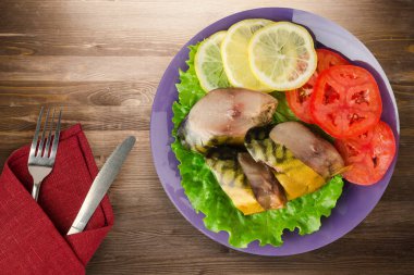 Mor tabakta füme uskumru. Çatal ve bıçak manzaralı. Kahverengi ahşap arka planda limonlu uskumru ve domates.