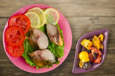 Sebze salatası manzaralı pembe tabakta tütsülenmiş uskumru. Kahverengi ahşap arka planda limonlu uskumru ve domates.