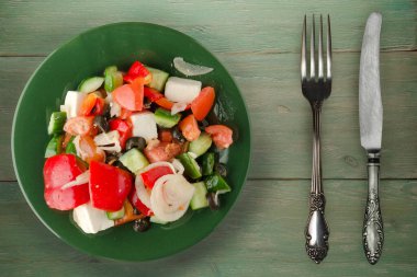 Yeşil ahşap arka planda Yunan salatası. Çatal ve bıçak manzaralı yeşil tabakta Yunan salatası. sağlıklı yiyecekler