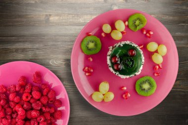 Kek ve meyve üzümleri, kivi, siyah ahşap zemin üzerinde nar. Pembe tabakta meyveli tatlı.