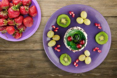 Kek ve meyve üzümleri, kivi, ahşap zemin üzerinde nar. Mor bir tabakta meyveli tatlı.