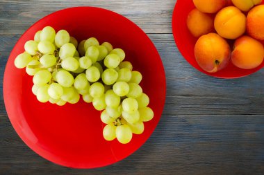 Mavi ahşap arka planda üzümler. Meyve salatası manzaralı kırmızı bir tabakta üzümler