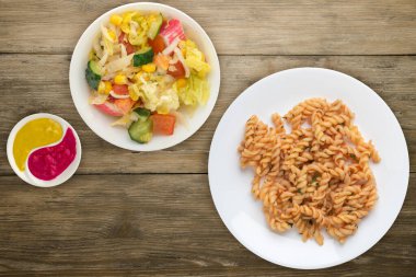 Tahta arka planda izole edilmiş beyaz bir tabakta makarna. Dereotlu domates soslu makarna. salata soslu makarna.