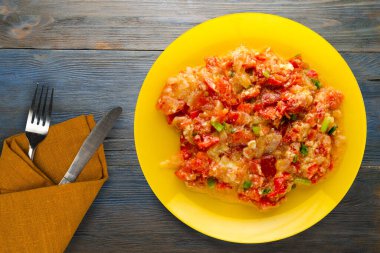 Mavi ahşap arka planda sarı tabakta soğanlı haşlanmış domates. Çatal ve bıçak manzaralı vejetaryen yemekleri.