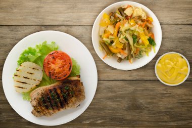pork grilled with potatoes and tomato on a wooden background. grilled pork on a white plate with salad top view