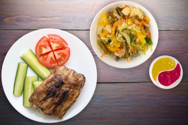 Dilimlenmiş salatalık ve domatesli ızgara domuz pirzolası. Mor ahşap arka planda domuz pirzolası. Kaburga ızgarası üst taraf görünümü